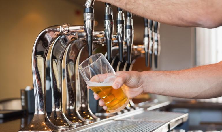 Persona che versa birra da un rubinetto in un bicchiere.