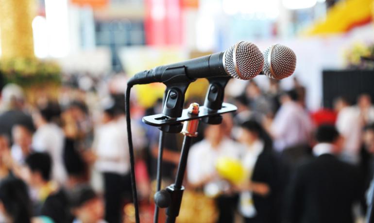 Due microfoni su un palco affollato in una conferenza.