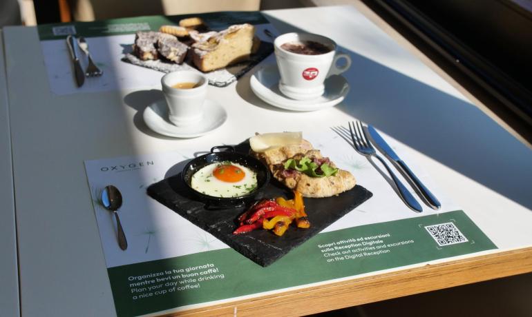 Colazione con uovo, pane e dolci su tavolo soleggiato.