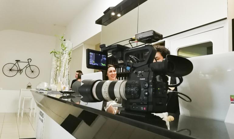 Telecamera professionale in un bar con persone sorridenti sullo sfondo.