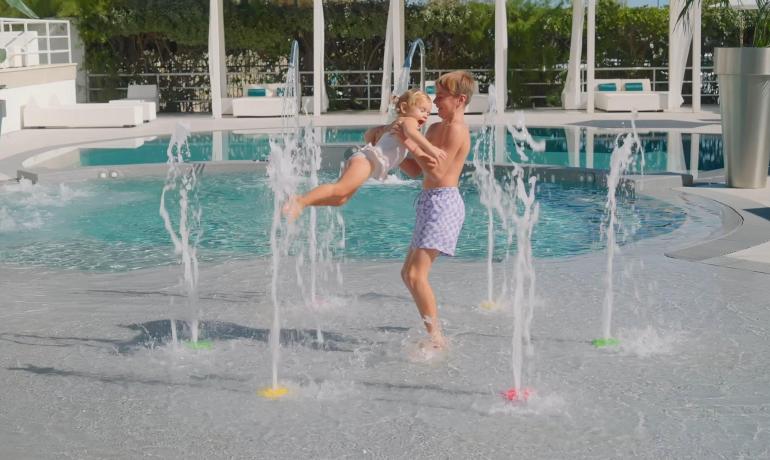 Bambini giocano felici in una fontana vicino alla piscina.