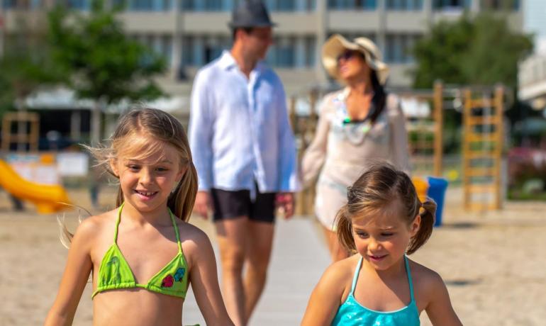 Bambini e genitori camminano sulla spiaggia in una giornata soleggiata.