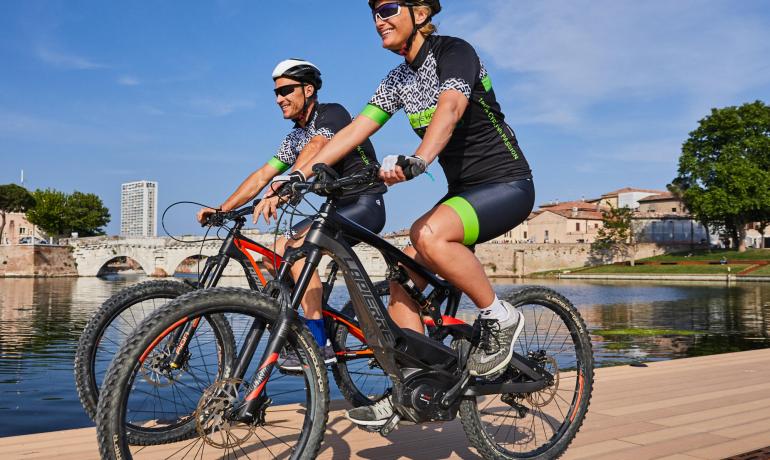 Zwei Radfahrer fahren an einem sonnigen Tag am Fluss entlang.